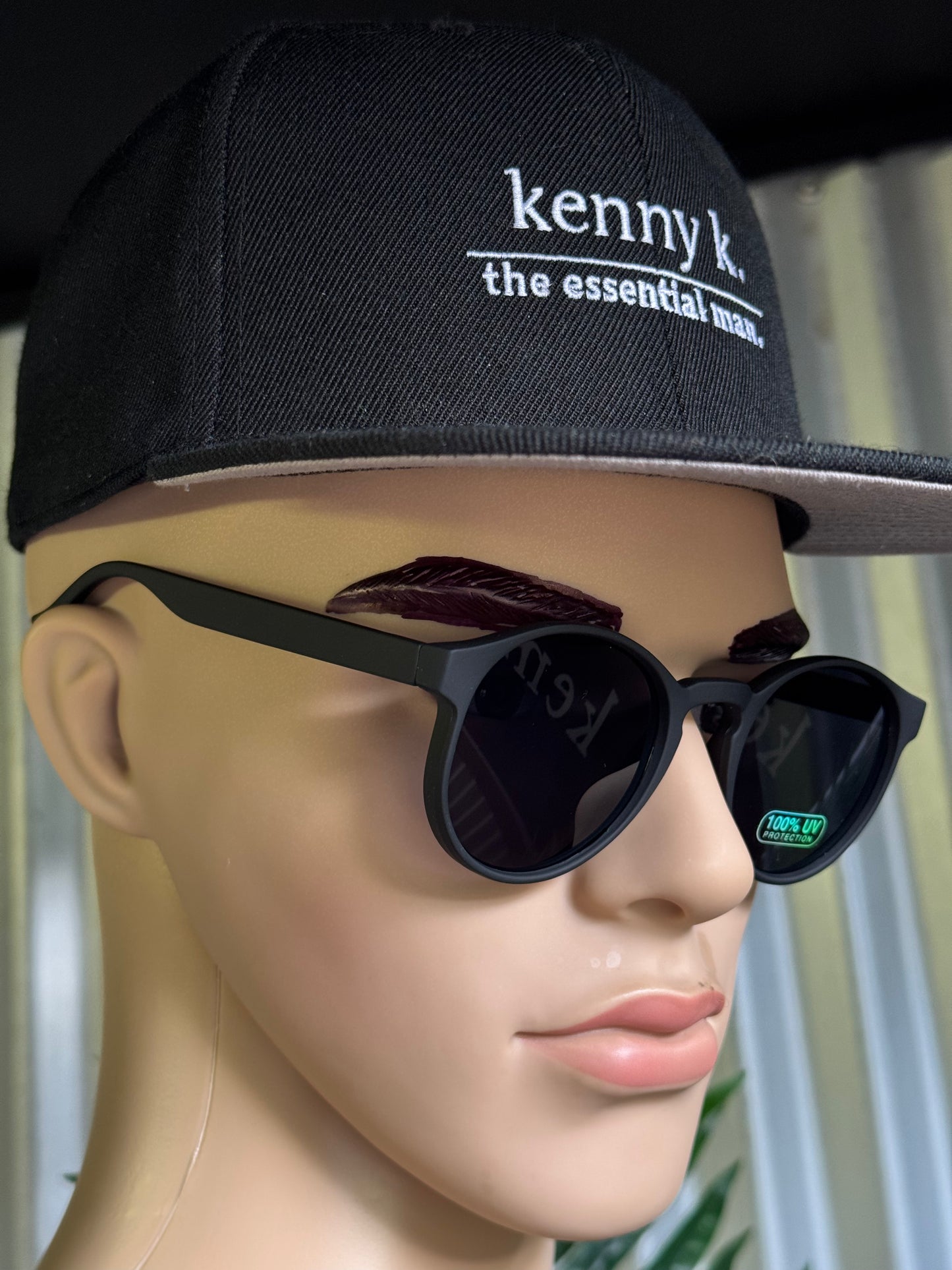 Mannequin head wearing a black cap with 'kenny k' branding and black sunglasses.